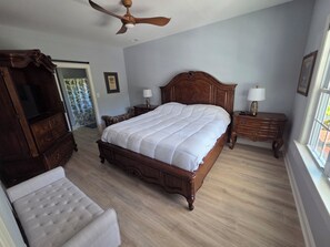 Een slaapkamer met een groot bed, een houten dressoir, een nachtkastje, een stoel en een plafondventilator.