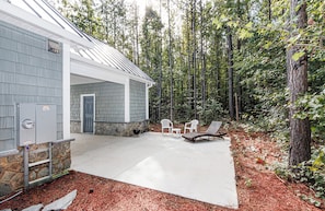 A house with a covered patio, stone walls, and a forested backdrop.