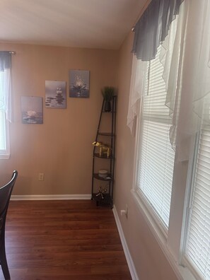 A room with wooden flooring, a window with blinds, a wall-mounted shelf with decorative items, and two framed pictures. - Tranquil 3-bedroom house w/ AC gated parking in charming Historic Selma, Alabama (Selma)