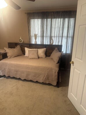 A bedroom with a bed, a nightstand, a lamp, and a window with curtains. - Tranquil 3-bedroom house w/ AC gated parking in charming Historic Selma, Alabama (Selma)