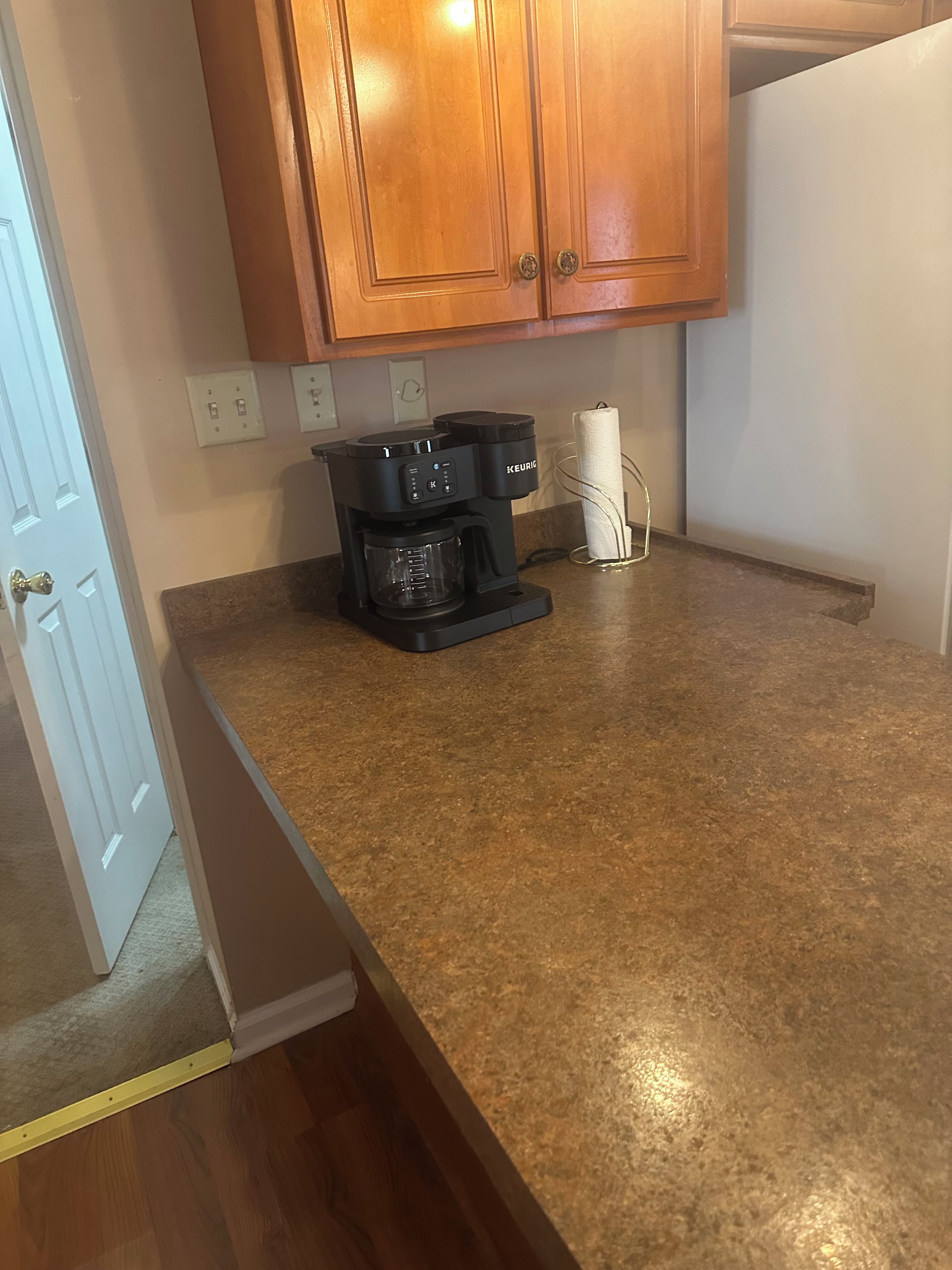 A kitchen with a coffee maker on the counter, wooden cabinets above, and a door with a brass handle.