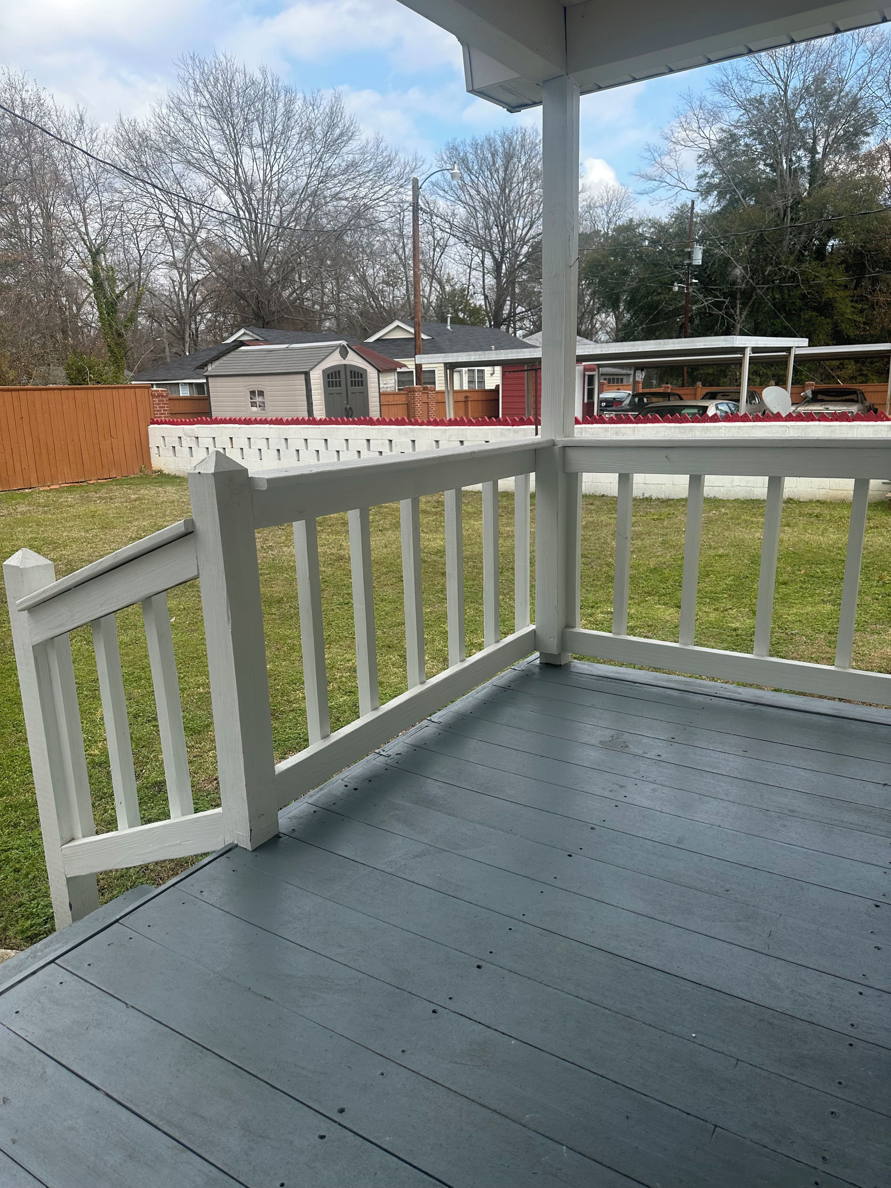 A covered deck with a white railing, a grassy yard, and a view of houses in the background.