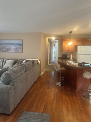 A modern living room with a grey sofa, a kitchen with wooden cabinets, and a view of the hallway. - Tranquil 3-bedroom house w/ AC gated parking in charming Historic Selma, Alabama (Selma)