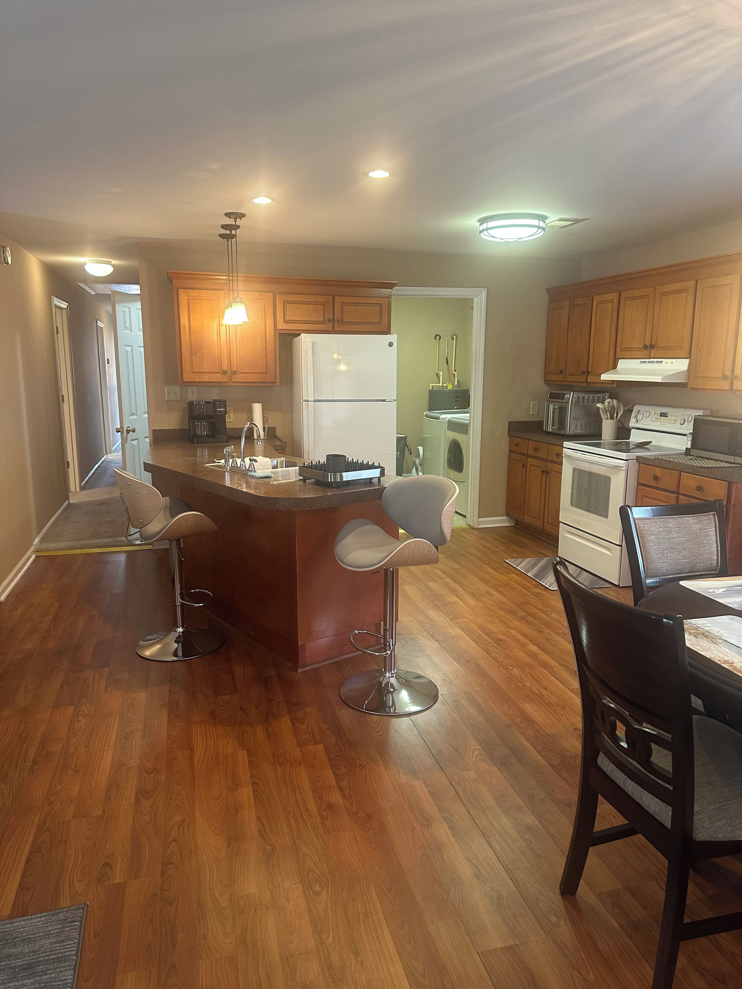 A modern kitchen with wooden cabinets, a central island with bar stools, a refrigerator, a microwave, and a stove.