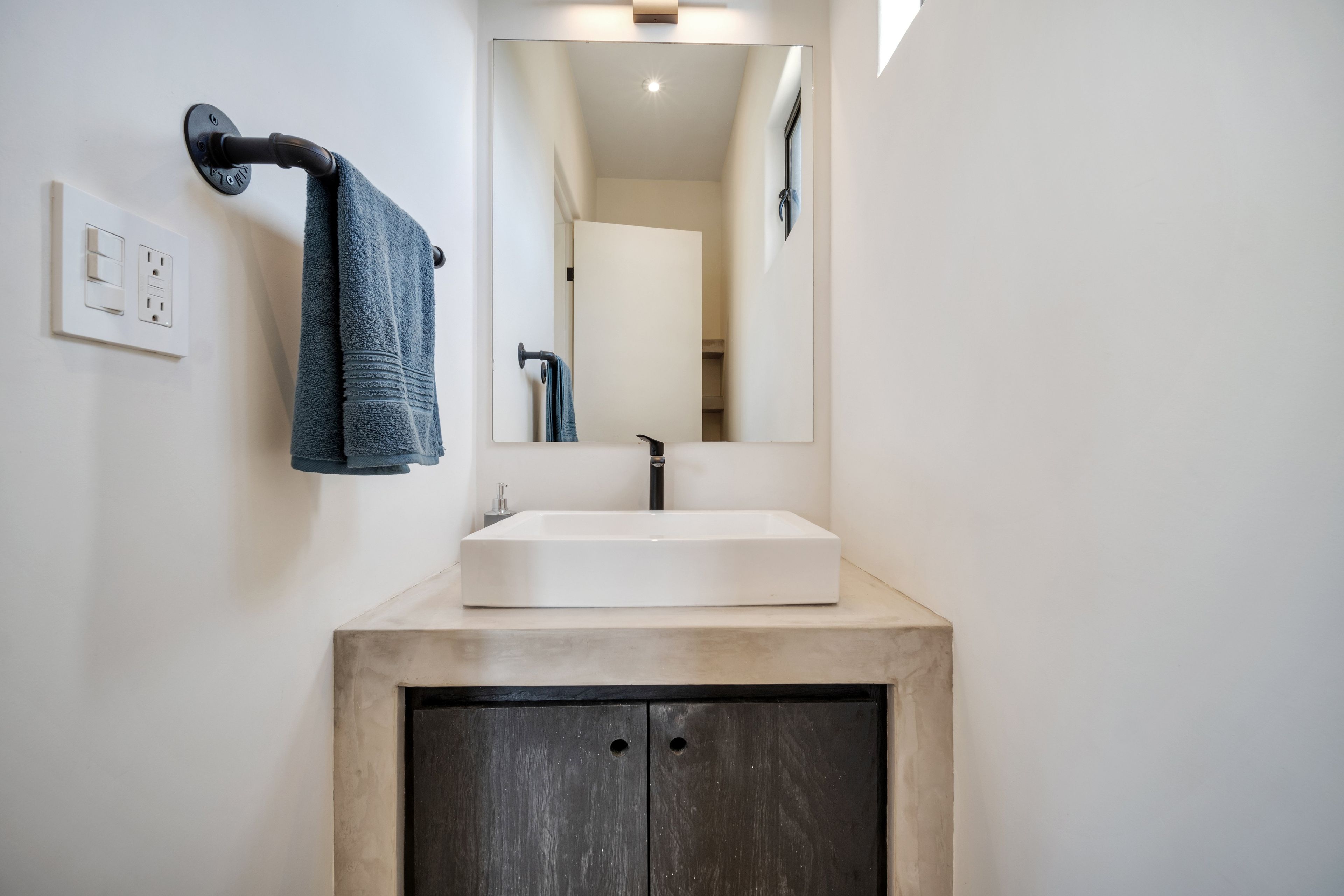 Un baño con un lavamanos blanco, un mueble de madera oscura y una toalla colgada en un gancho.