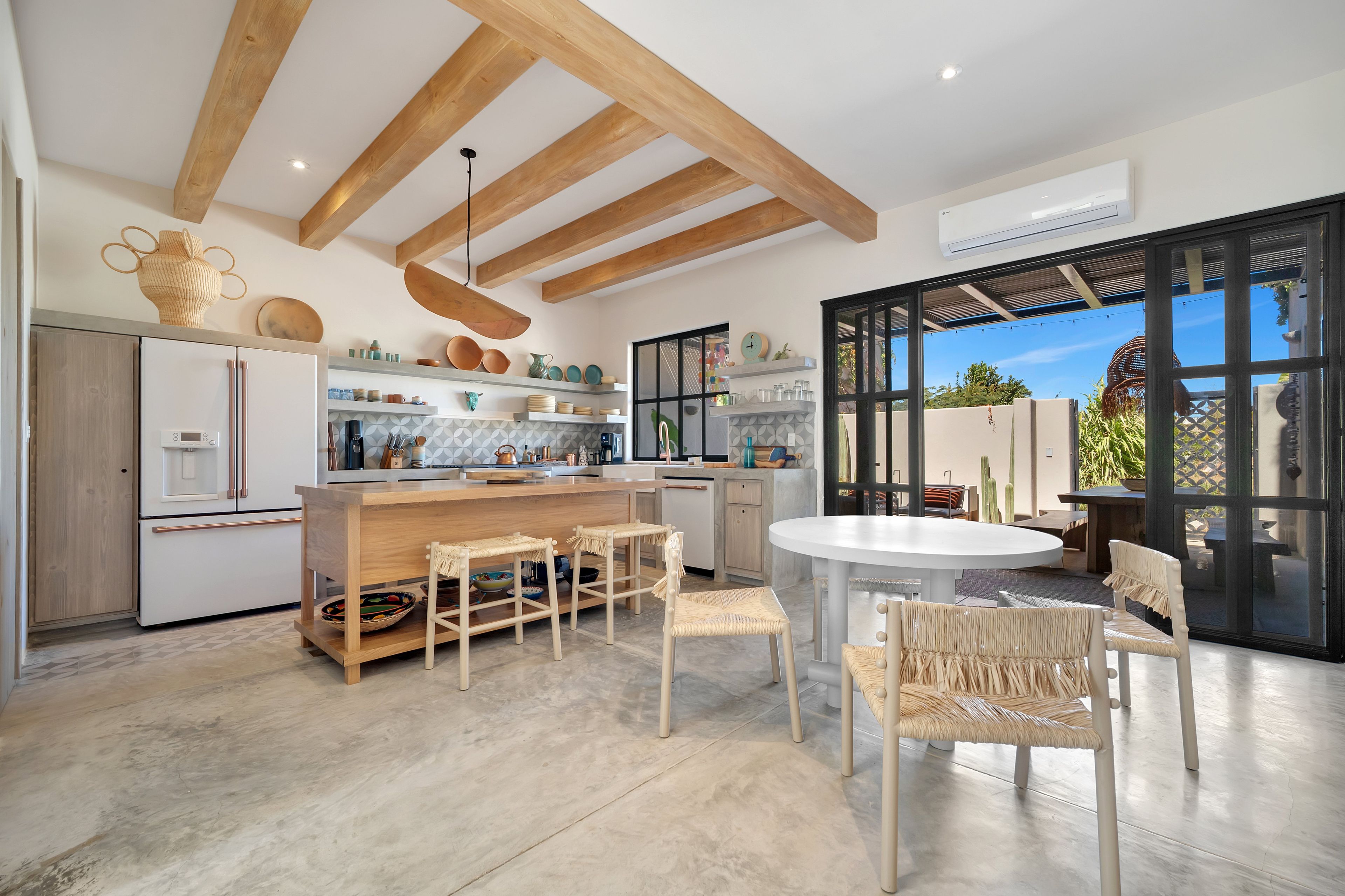 A modern kitchen with wooden beams, a central island, and a dining area with wicker chairs.