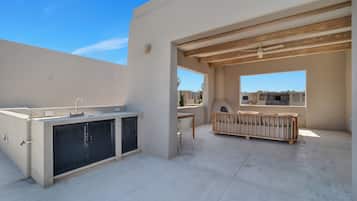 Un patio al aire libre con cocina integrada, un banco de madera y vista a edificios vecinos.