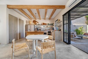 A modern kitchen with wooden beams, a dining area with wicker chairs, and a view of the outdoors.