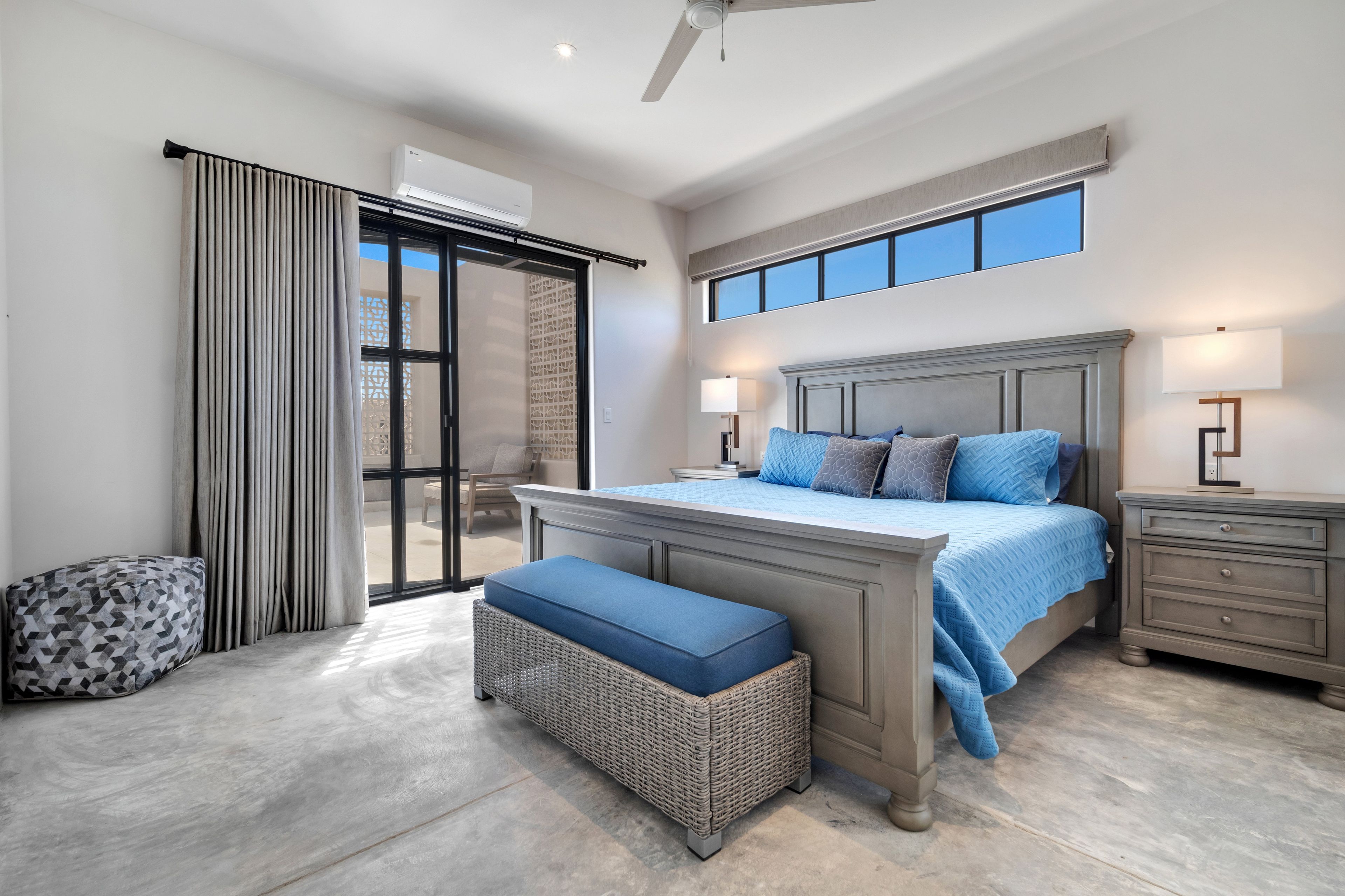 A bedroom with a large bed, a nightstand, a bench, a window, and an air conditioning unit.