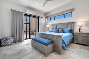 Een slaapkamer met een groot bed, een nachtkastje, een bankje, een raam en een airconditioning.
