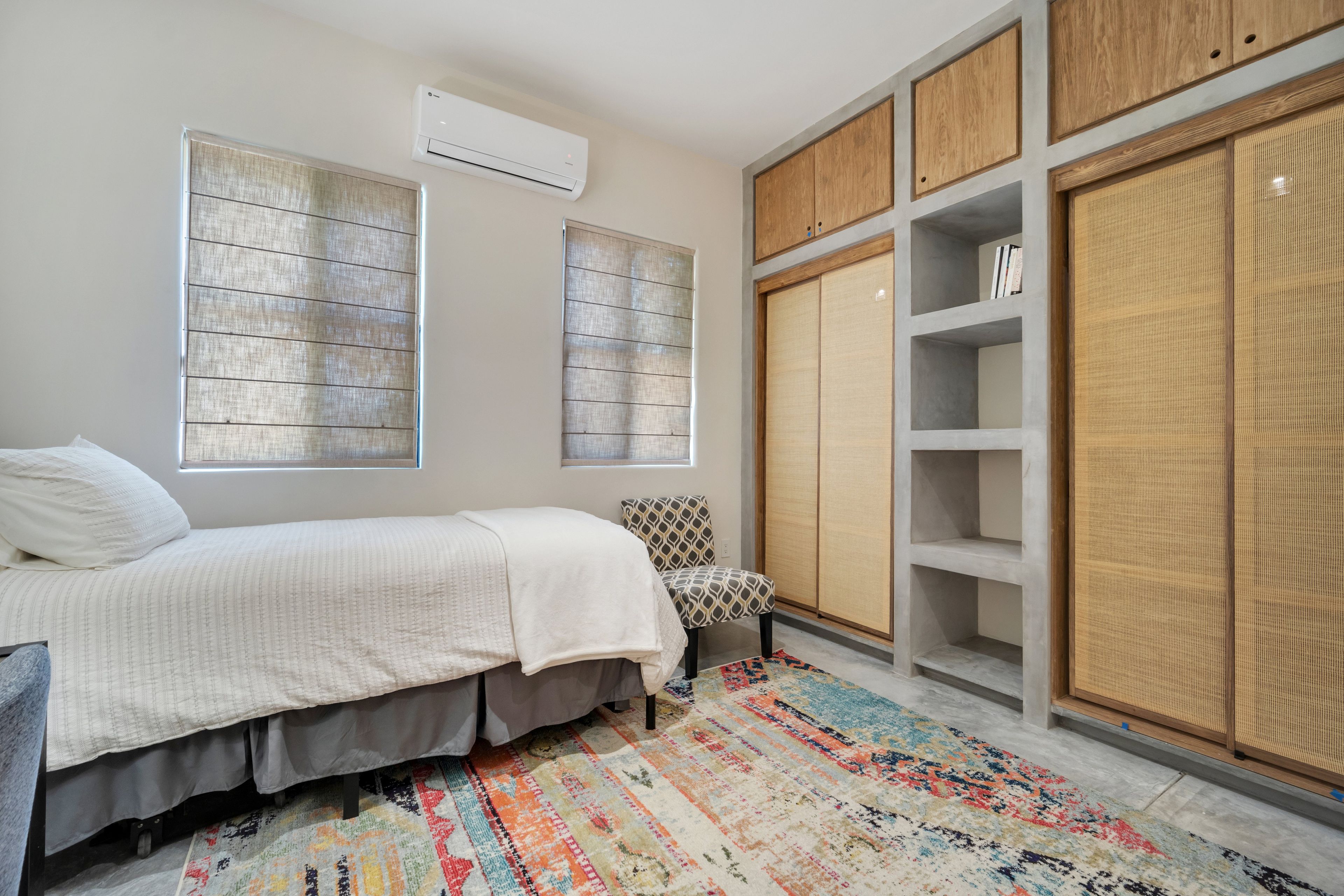 A bedroom with a bed, a chair, a wardrobe, and a window.