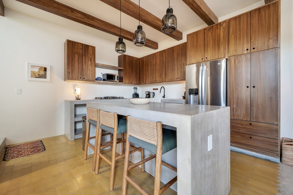 Een moderne keuken met houten kastjes, een centraal eiland met barkrukken, een ingebouwde magnetron en een roestvrijstalen koelkast.