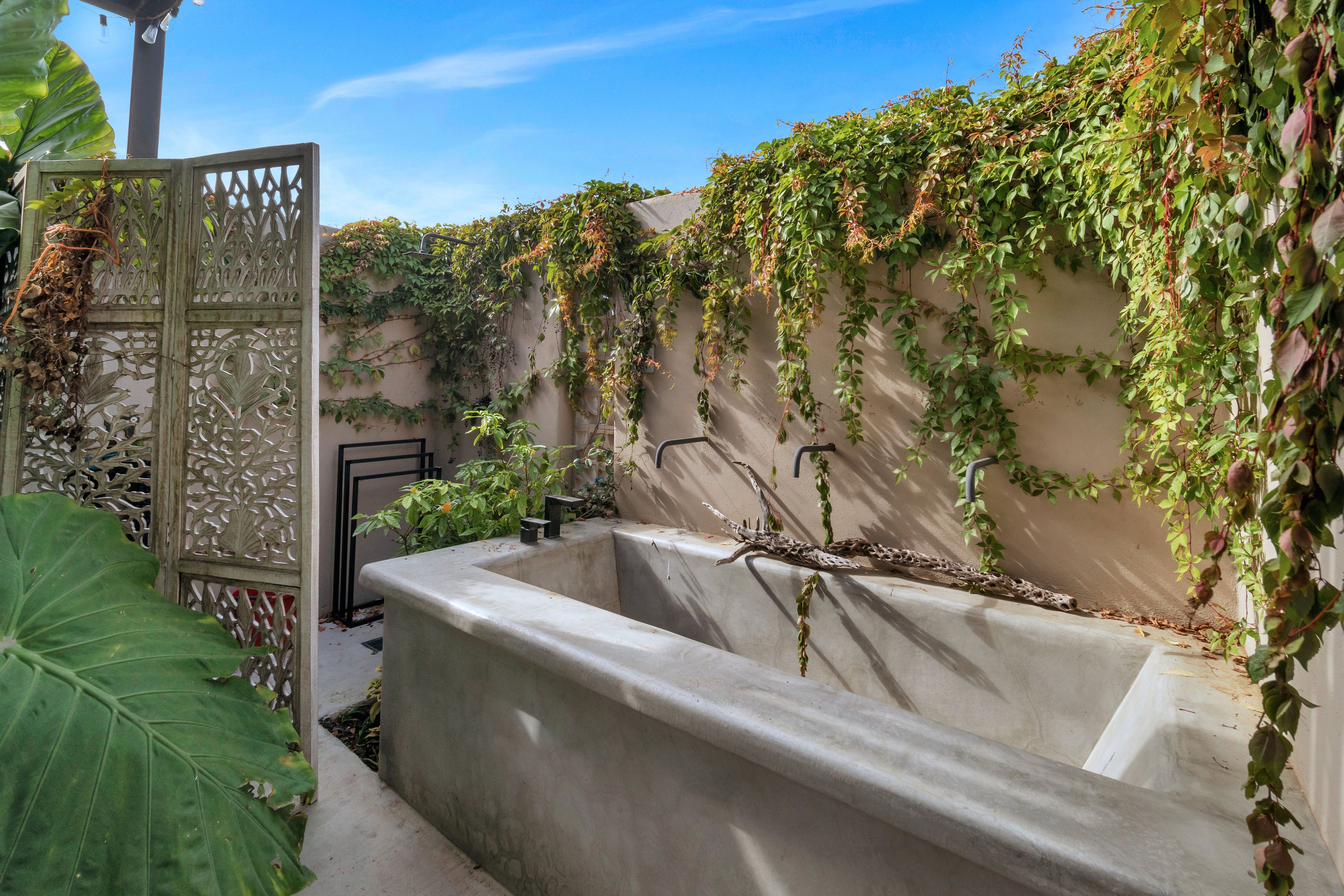 A concrete planter with a water feature, surrounded by greenery and a decorative metal gate.