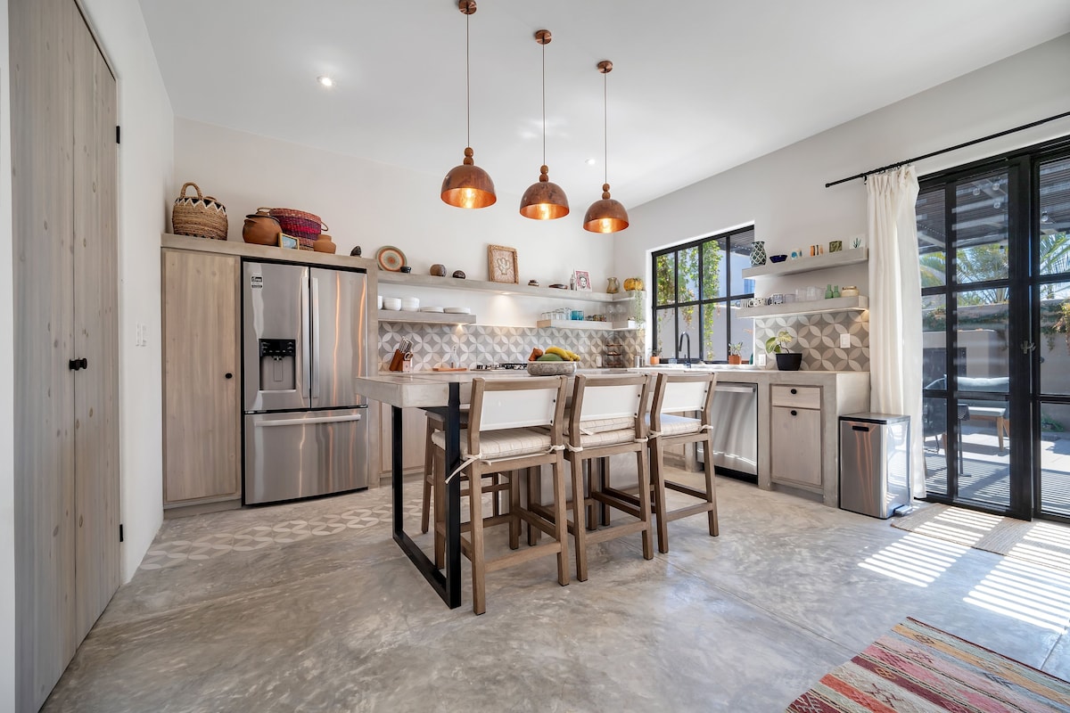 Een moderne keuken met een centraal eiland, roestvrijstalen apparatuur en hanglampen.