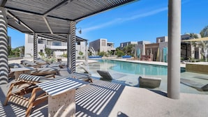 Zona junto a la piscina con sillones de descanso y un área de estar techada.
