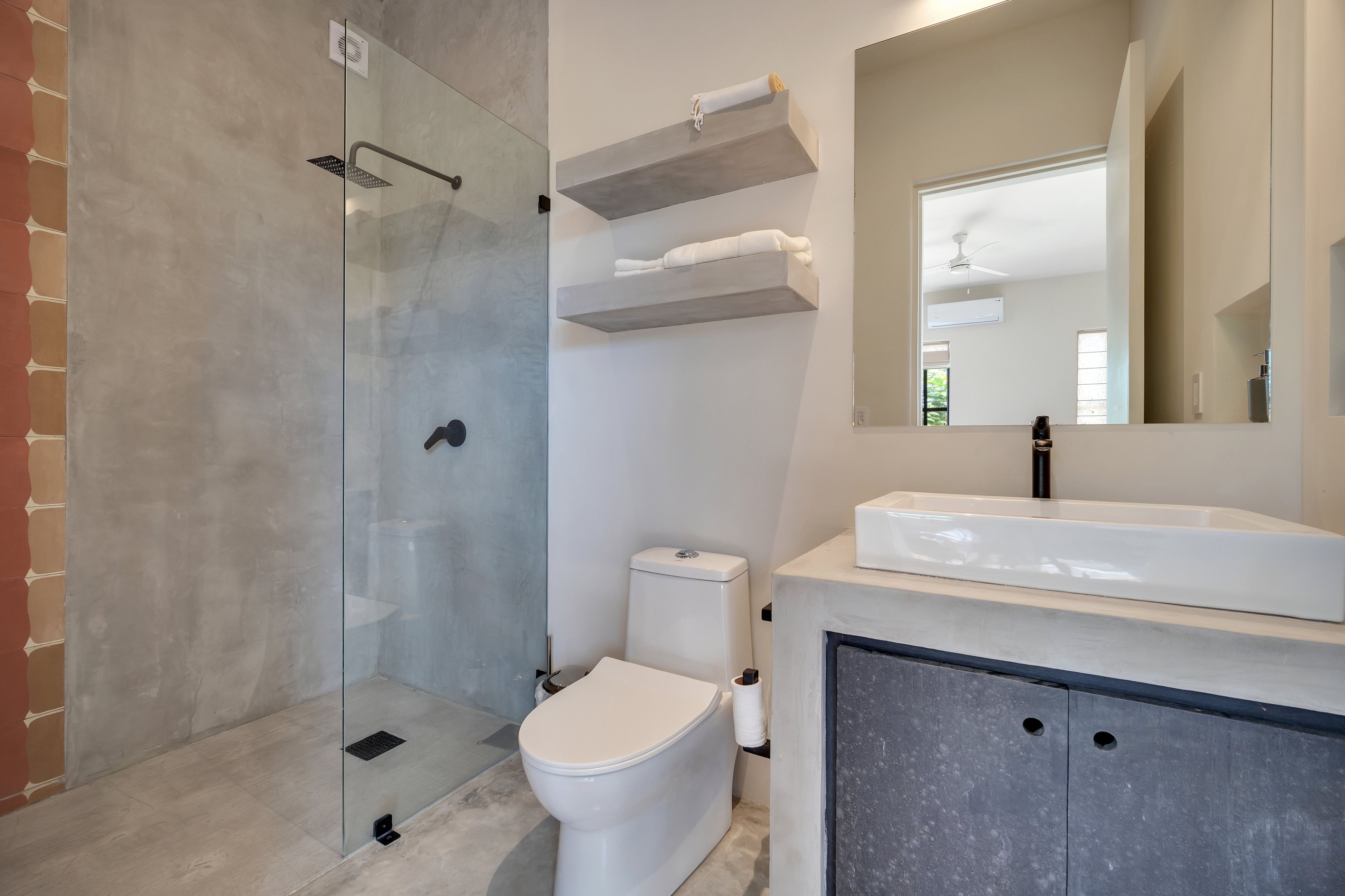 Un baño moderno con ducha envuelta en vidrio, inodoro, lavamanos con espejo y estantes integrados.