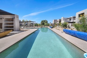 A clear swimming pool with lounge chairs and umbrellas, surrounded by modern buildings and greenery. - Baja Sage (El Pescadero)