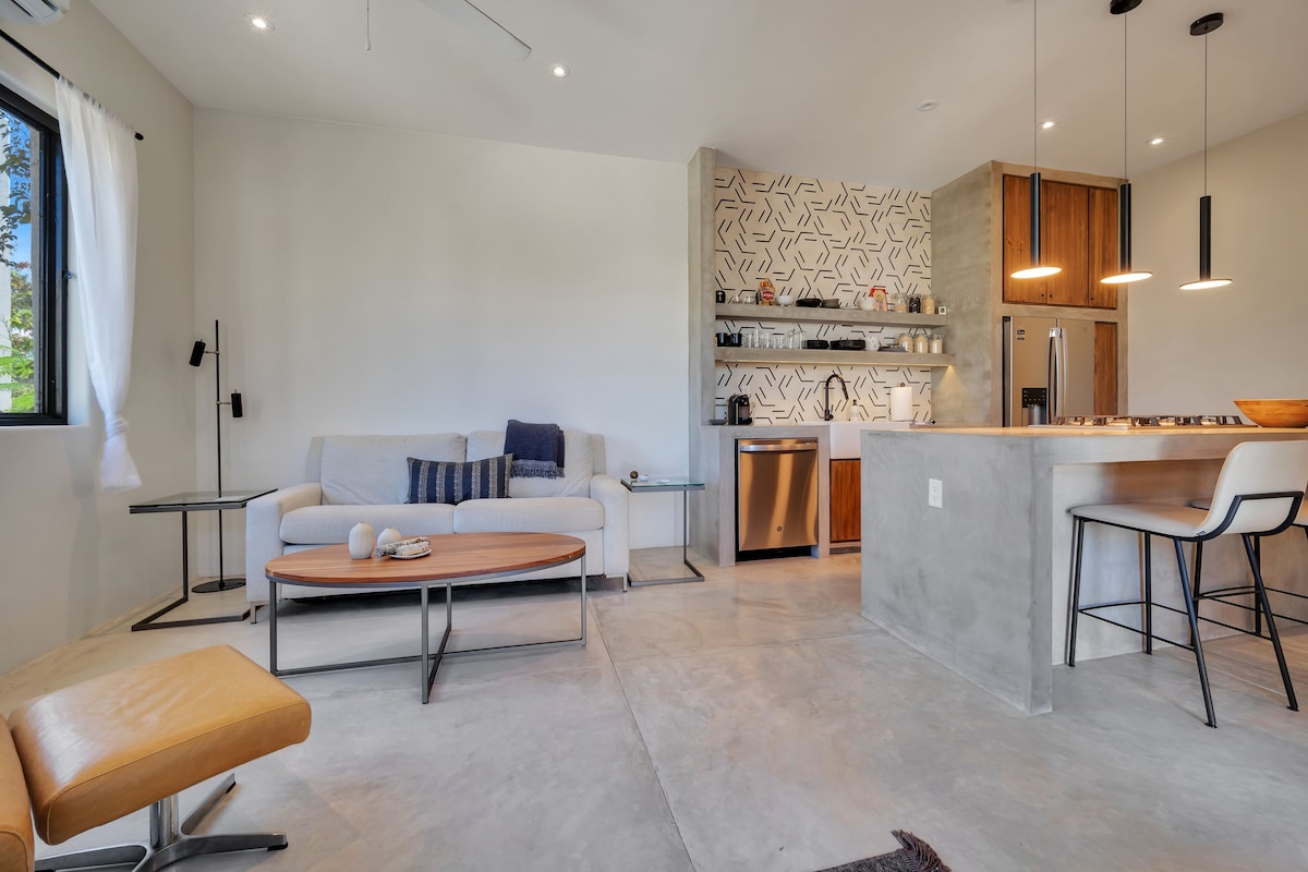 Een moderne keuken met een centraal eiland, inbouwapparatuur en een eethoek met een barkruk.