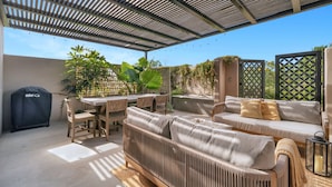 Un patio exterior con una zona de estar cubierta, una parrilla y una mesa con sillas.