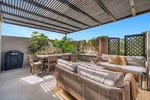 Een terras buiten met een overdekte zithoek, een barbecue en een tafel met stoelen.