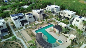 Een wooncomplex met meerdere moderne huizen, een zwembad en zonnepanelen op de daken.
