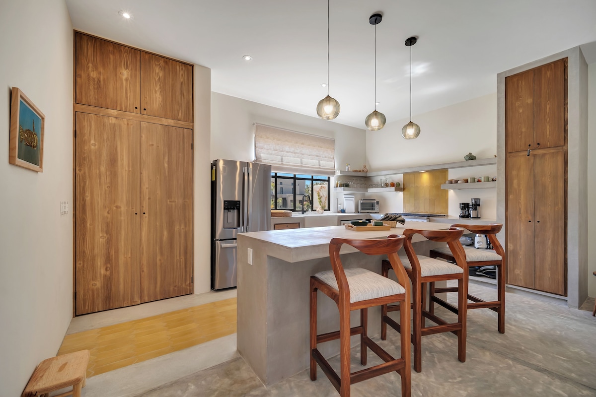 Een moderne keuken met houten kastjes, een roestvrijstalen koelkast en een centraal eiland met barkrukken.