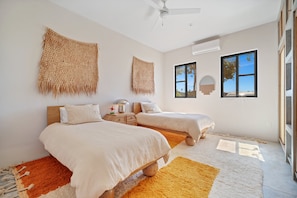A bedroom with two beds, a ceiling fan, and a large window with a view. - Baja Sage (El Pescadero)