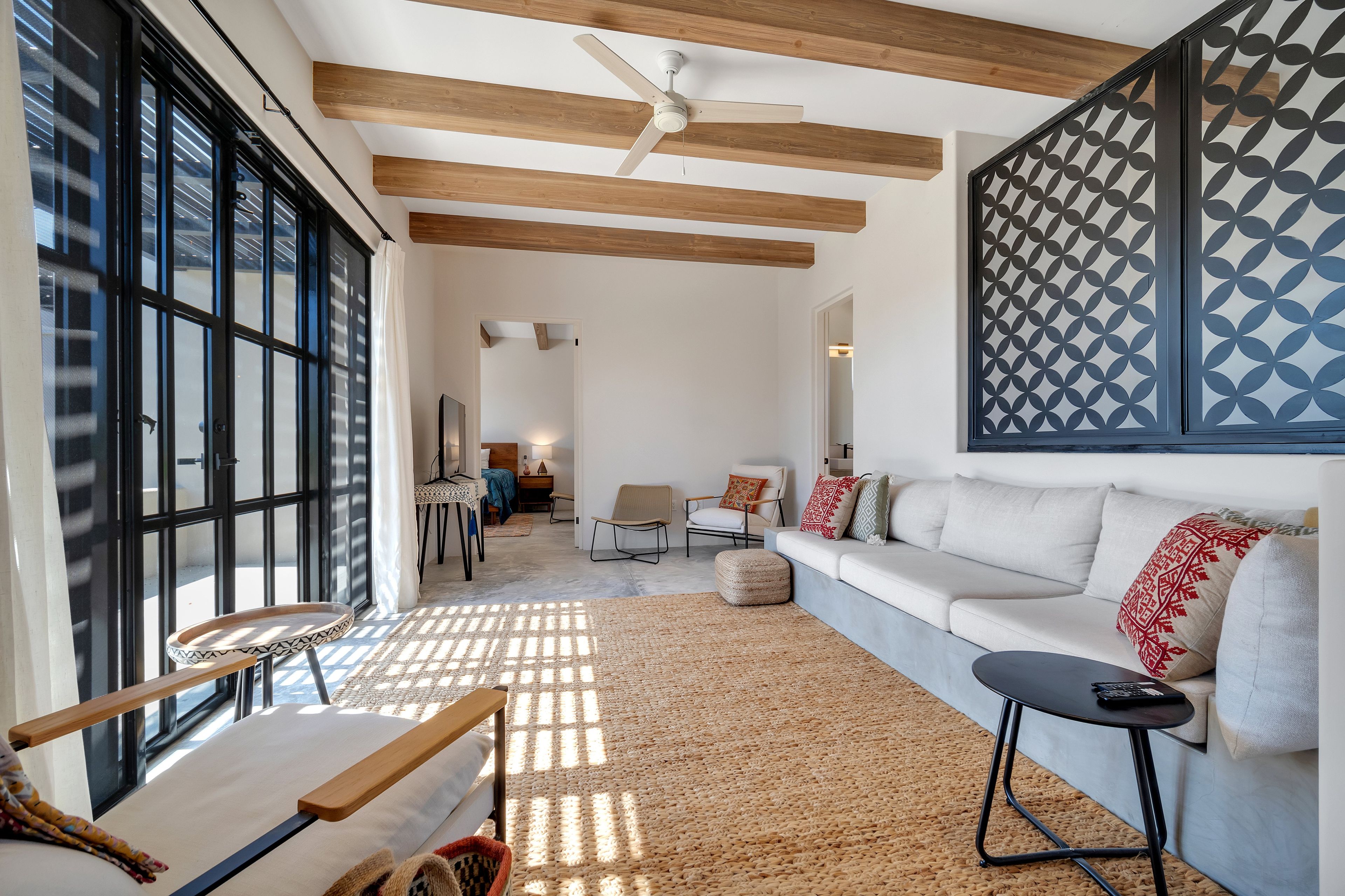 Una sala moderna con un ventanal grande, un ventilador de techo, un sofá, una mesa de centro y una pared con diseño.