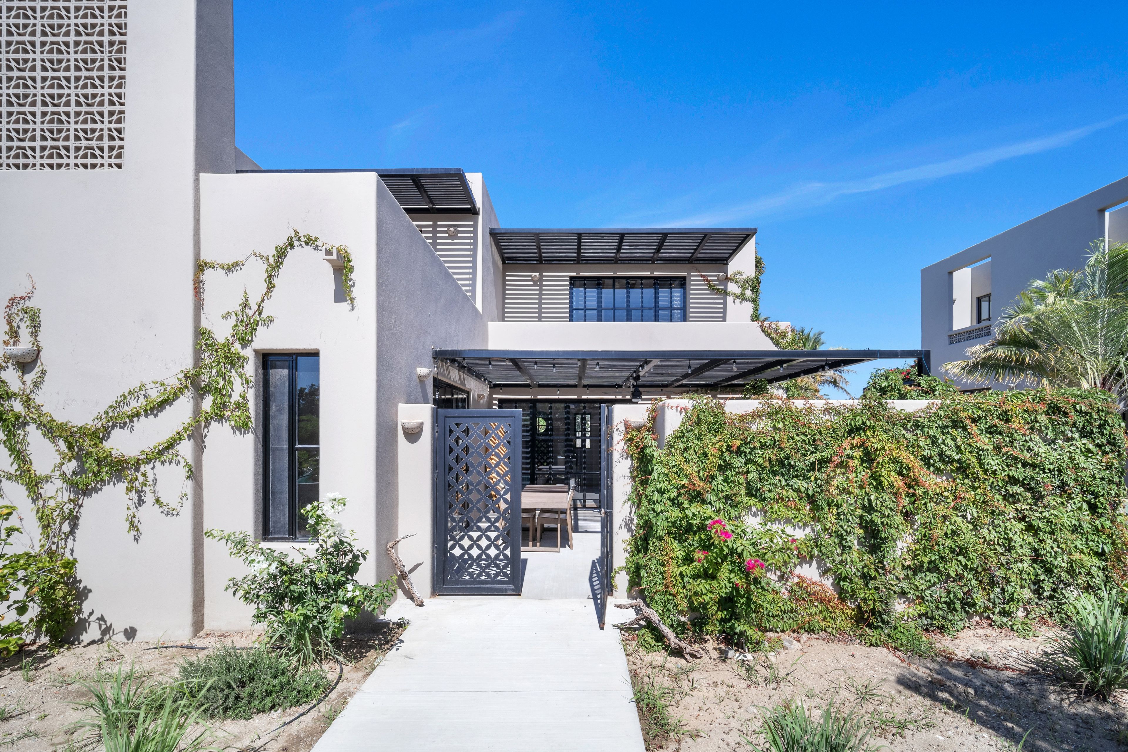 A modern house with a covered patio, a concrete pathway, and a variety of plants.