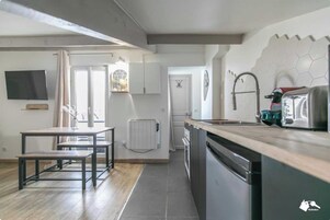 A modern kitchen with a dining area, a built-in dishwasher, and a window with curtains.