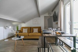 A cozy living area with a sofa, a dining table set for two, and a window with curtains. - Charming Apartment - 1ch/4p - Montreuil (Montreuil)