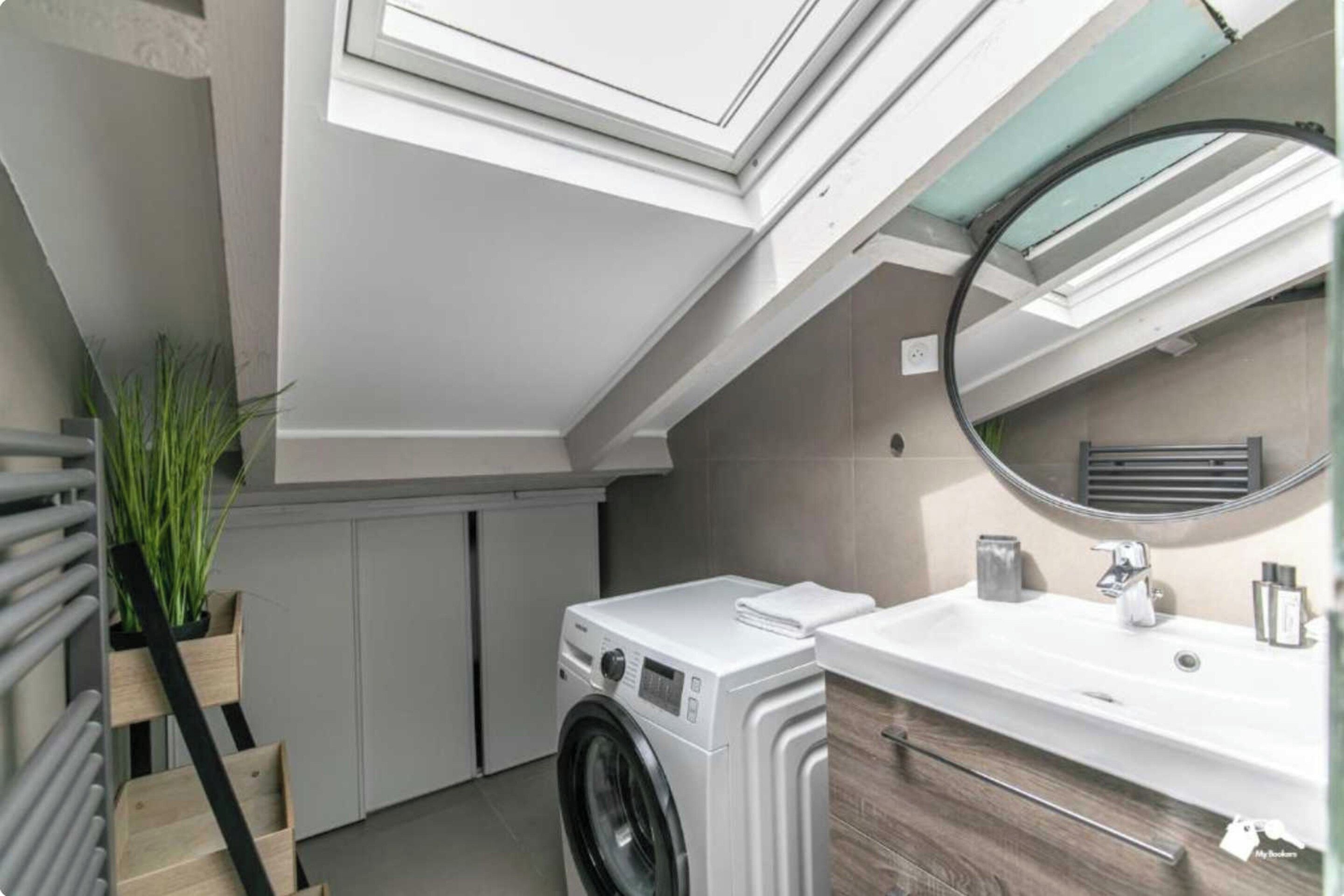 A compact laundry room with a washing machine, a sink, and a mirror.