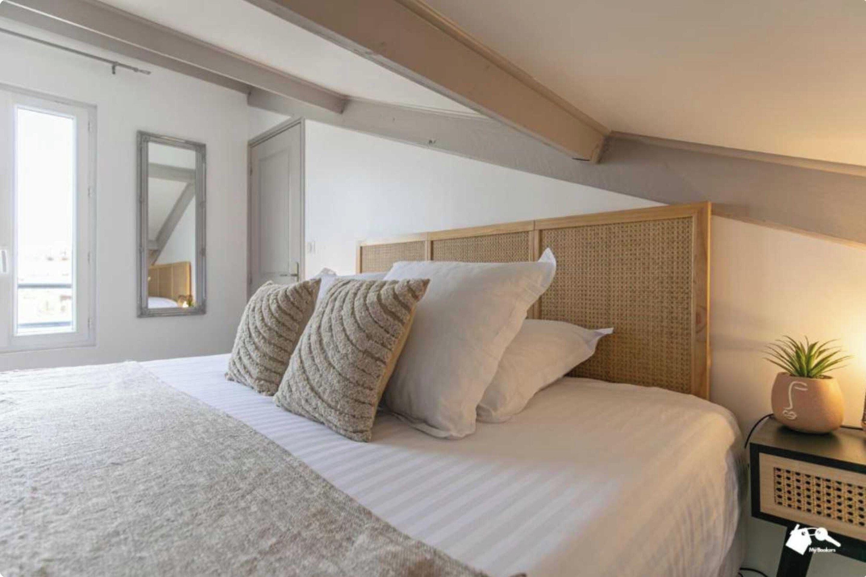 Une chambre à coucher avec un grand lit, une tête de lit, une table de chevet agrémentée d’une plante et un miroir au mur.