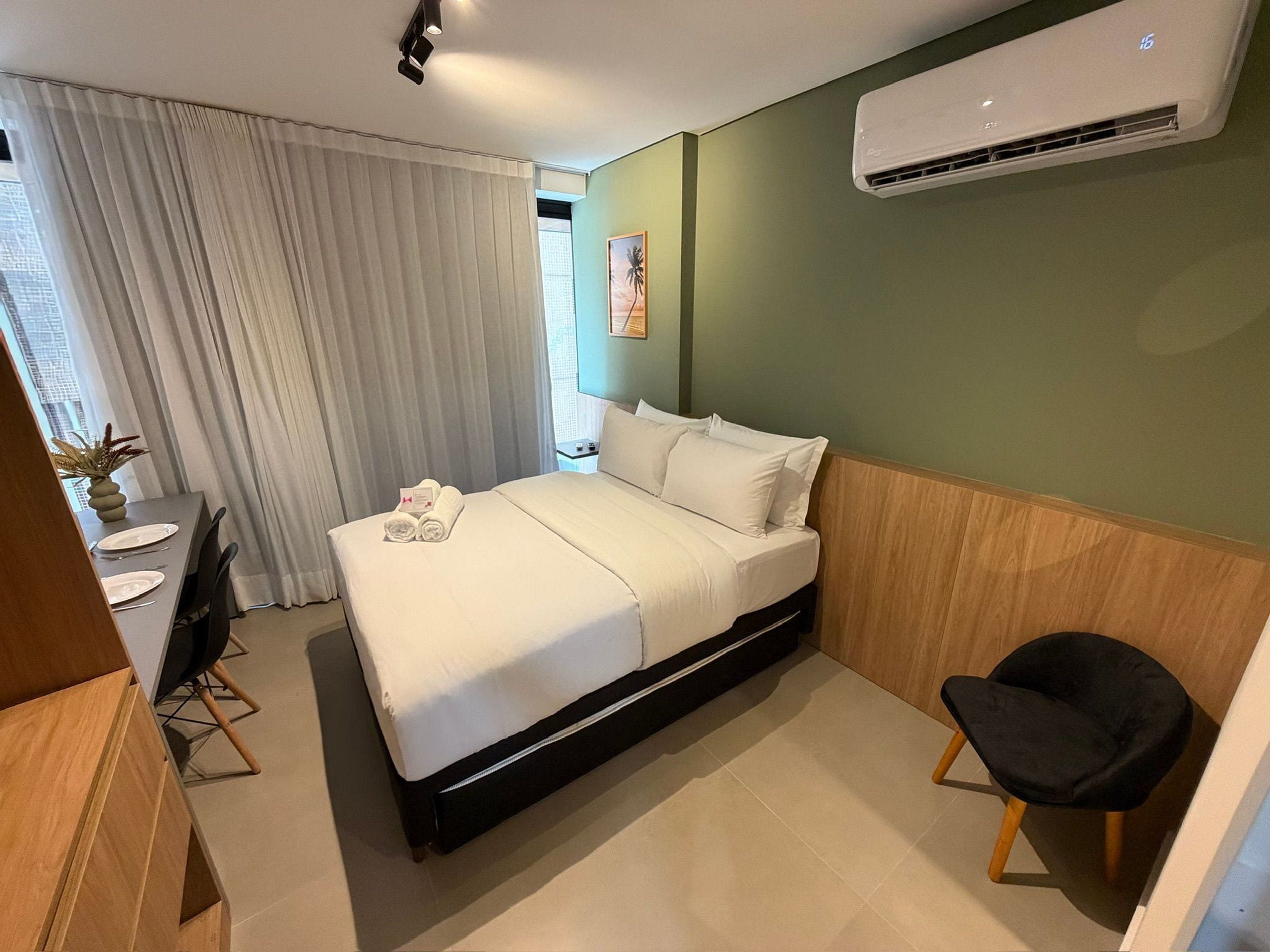 A hotel room with a bed, a desk, a chair, and an air conditioning unit.