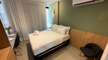 A hotel room with a bed, a desk, a chair, and an air conditioning unit.