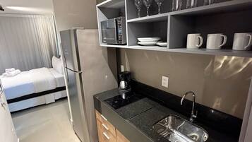 Una cocina compacta con microondas, cafetera y lavamanos.