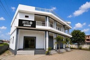 A modern hotel with a prominent sign, a balcony, and a paved entrance.