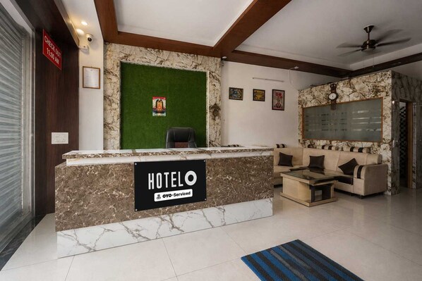 A hotel reception area with a marble counter, a green artificial grass wall, and a sofa set.