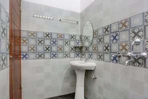 A bathroom with a white pedestal sink, a mirror, a towel rack, and a shower with a chrome faucet.