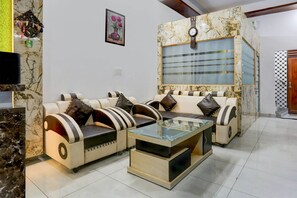 A living room with a sofa set, a glass coffee table, and a wall-mounted clock.