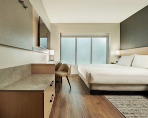 A hotel room with a bed, desk, chair, and a large window.