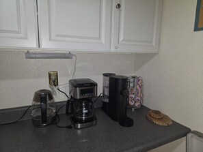 A kitchen counter with a coffee maker, a glass carafe, a coffee grinder, and a coffee pod holder. - Serenity Lodge:5BR w/AC,5 Min/Town/Golf/Train (Williams)