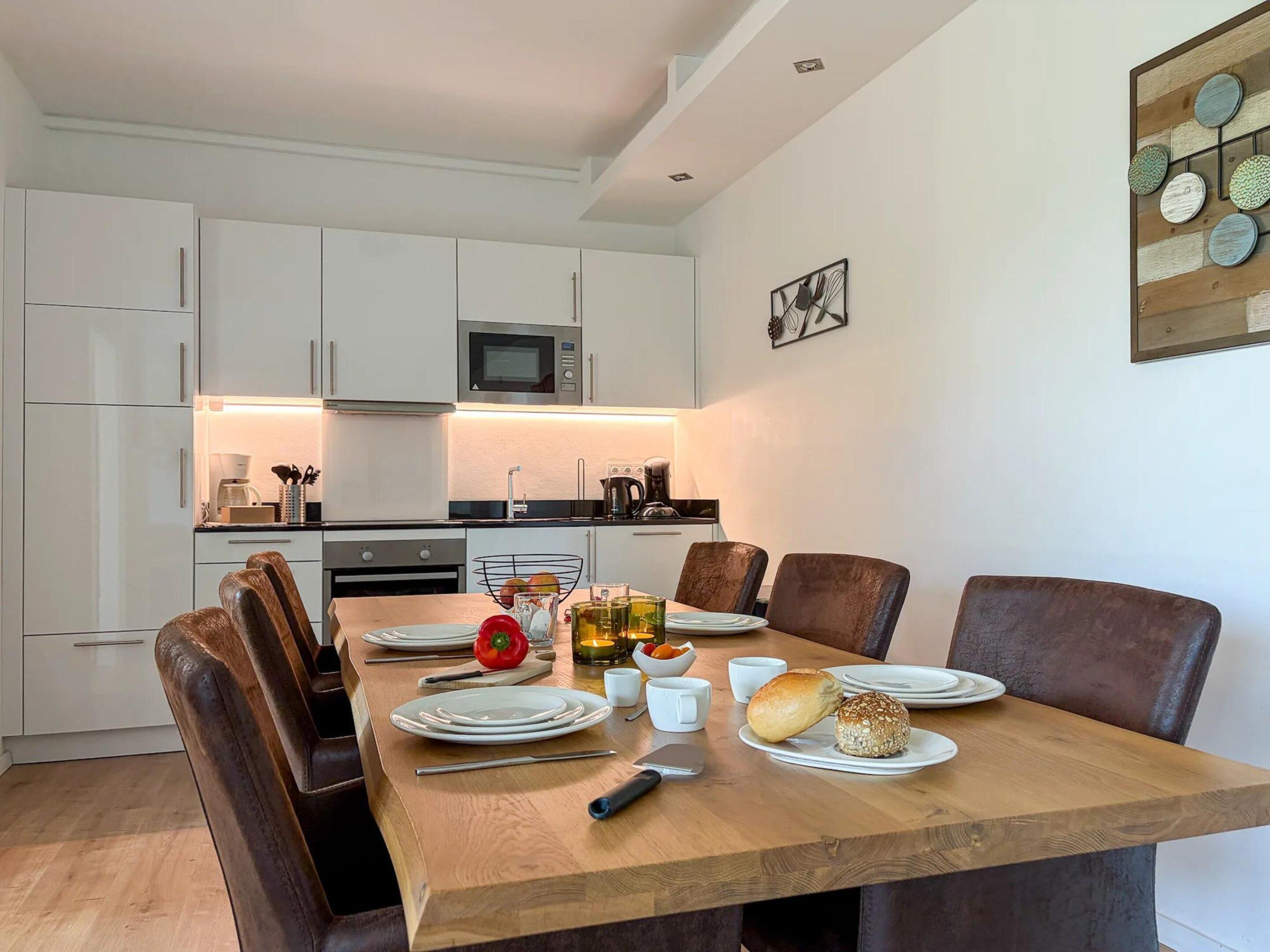 A modern kitchen with white cabinets, a microwave, and a dining area with a wooden table set for four.