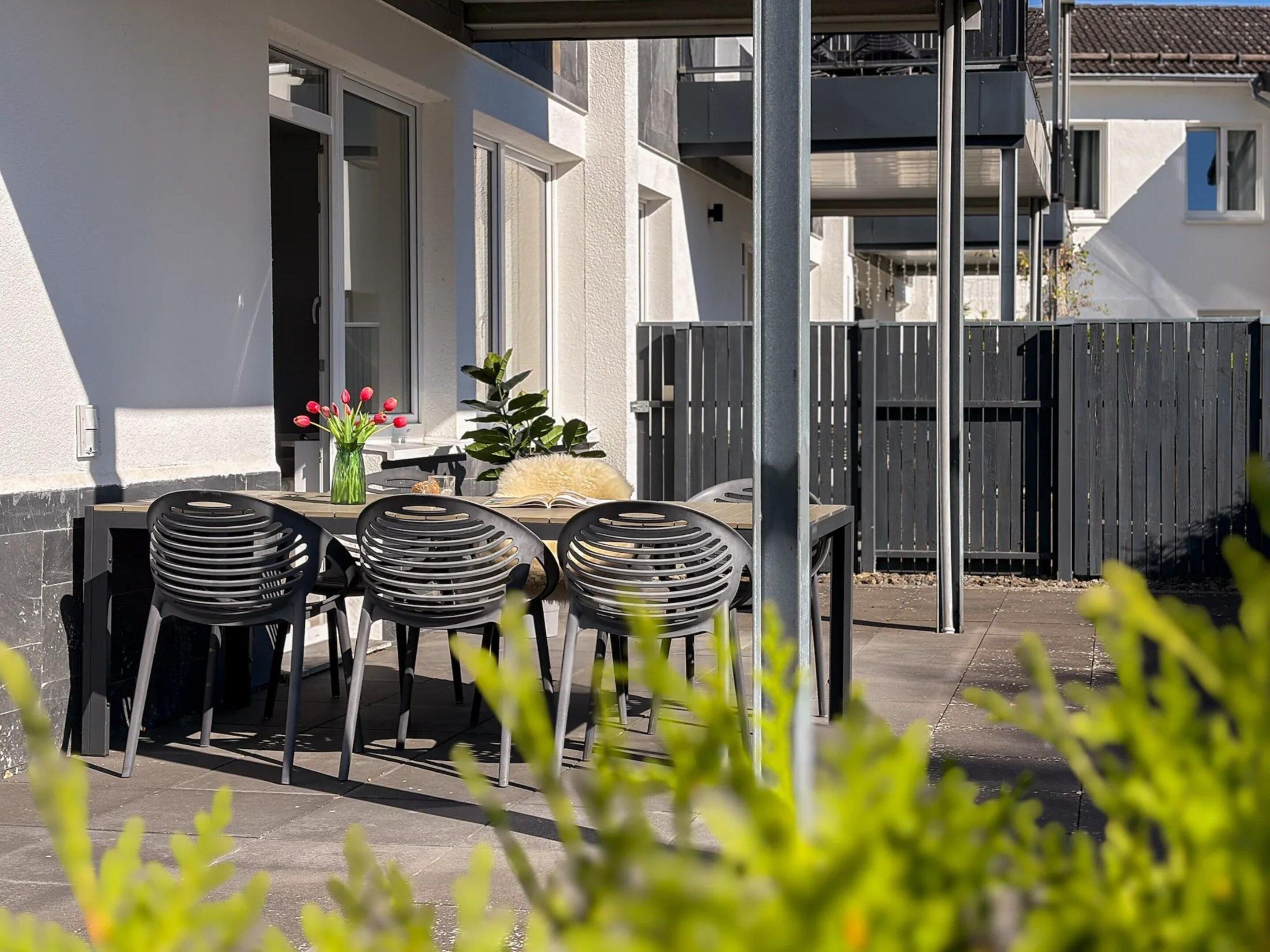 Une terrasse extérieure avec une table et des chaises, une clôture en bois et un bâtiment en arrière-plan.