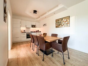A modern kitchen with white cabinets, a wooden dining table, and a wall-mounted art piece. - Modern Apartment Retreat for 6 in Winterberg Zuschen (Schmallenberg)