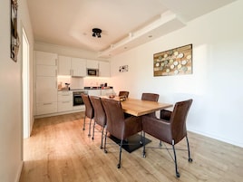 Una cocina moderna con armarios blancos, una mesa de comedor de madera y una obra de arte colgando en la pared.