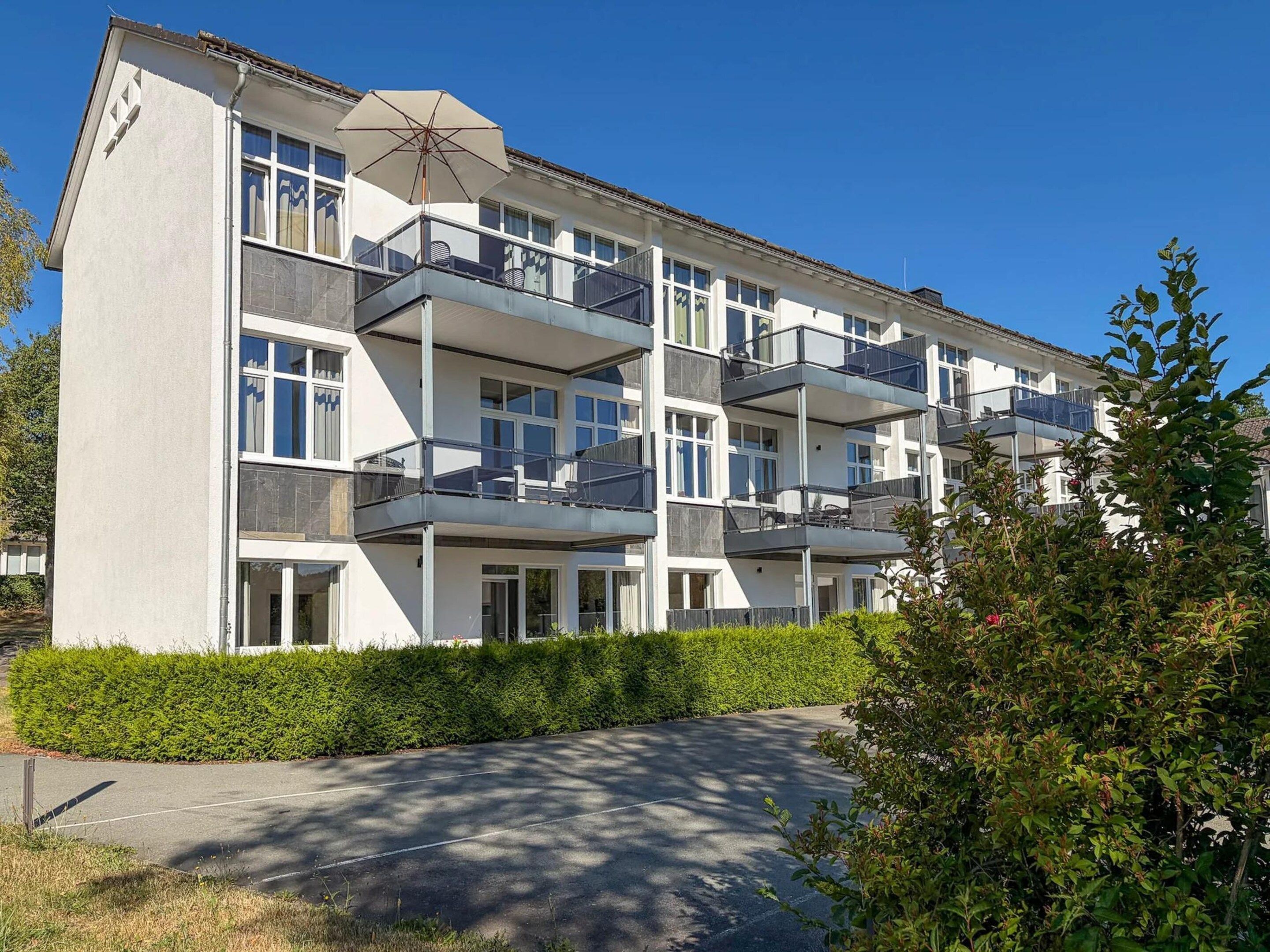 Un edificio residencial de varios pisos con balcones, un espacio de estar al aire libre techado y un jardín bien cuidado.