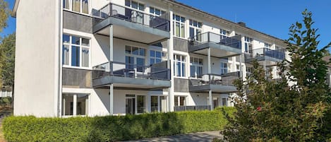 Un edificio residencial de varios pisos con balcones, un espacio de estar al aire libre techado y un jardín bien cuidado.