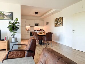 A modern living room with a dining area, a kitchen in the background, and a potted plant. - Modern Apartment Retreat for 6 in Winterberg Zuschen (Schmallenberg)