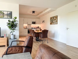 Una sala de estar moderna con comedor, cocina al fondo y una planta en maceta.